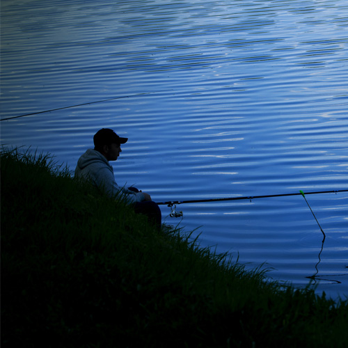 a man sitting on a shore fishing at night
